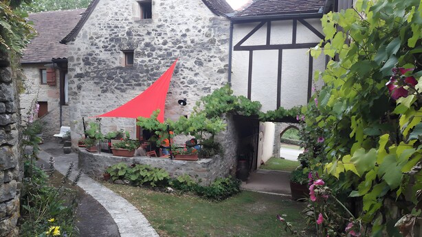 Un edificio de piedra con techo inclinado, toldo rojo y plantas en macetas.