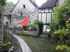 Un edificio de piedra con techo inclinado, toldo rojo y plantas en macetas.