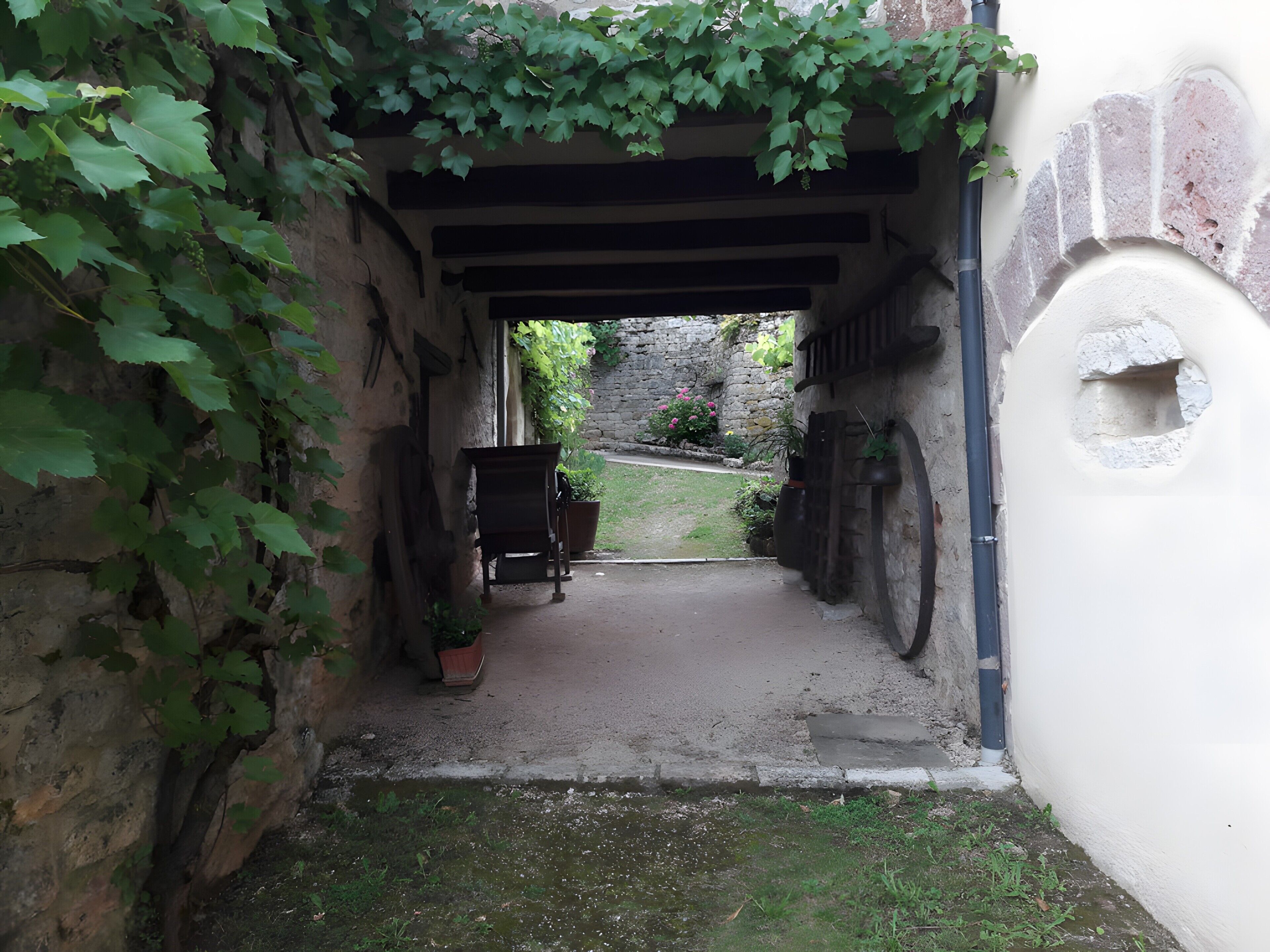 Une ruelle étroite, avec un banc en bois et des plantes en pot, qui mène à un mur de pierre et à une porte blanche.