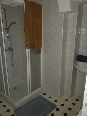 Un baño con ducha envuelta en vidrio, un lavamanos y un suelo estampado.
