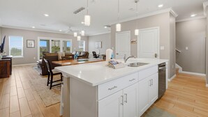 A modern kitchen with a large island, white cabinetry, and pendant lighting. - Sandy Feet Retreat at Lost Key Villas (Pensacola)