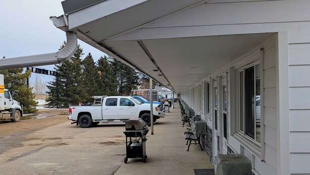 Un espacio al aire libre cubierto con una fila de bancos, un carrito de parrilla y vehículos estacionados.