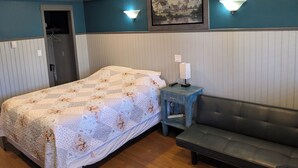 Un dormitorio con cama, mesita de noche, lámpara y un sofá.