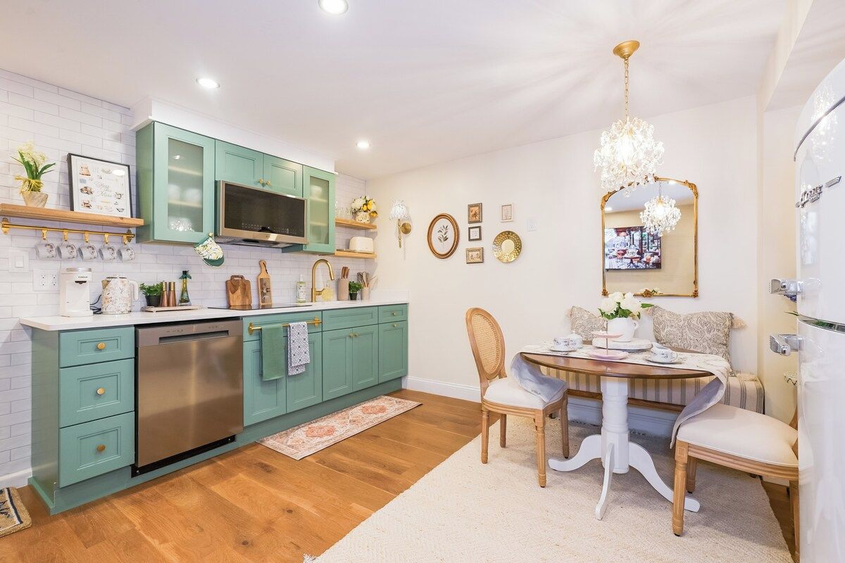 A modern kitchen with teal cabinets, stainless steel appliances, and a dining area with a chandelier.
