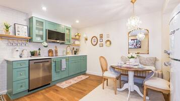 A modern kitchen with teal cabinets, stainless steel appliances, and a dining area with a chandelier.