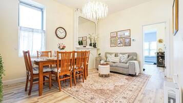 A dining area with a wooden table and chairs, a chandelier, and a large mirror above the table.