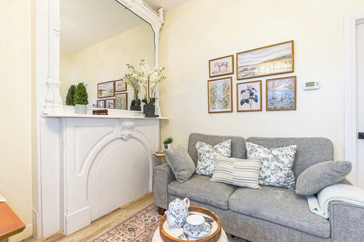 A cozy living room with a grey sofa, a white fireplace mantel, and framed artwork on the wall.