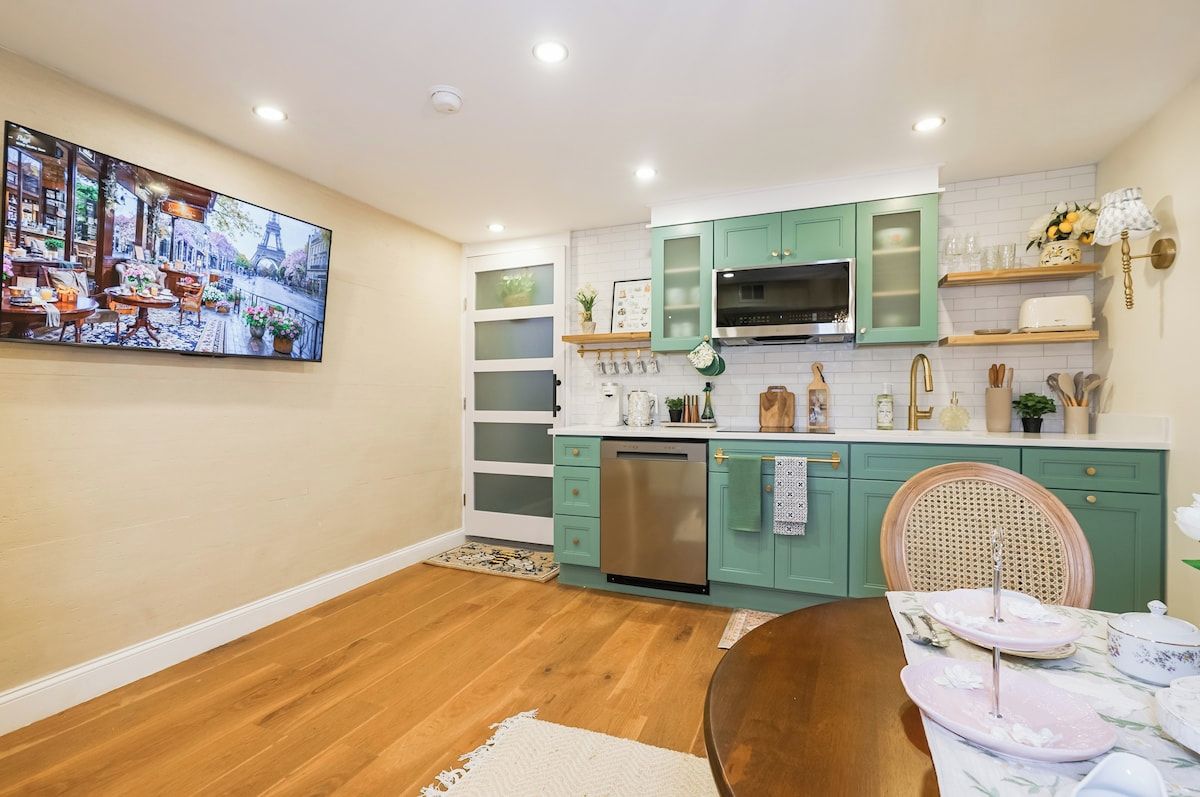 A modern kitchen with teal cabinets, a stainless steel dishwasher, and a dining area with a wooden table and chairs.