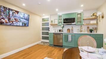 A modern kitchen with teal cabinets, a stainless steel dishwasher, and a dining area with a wooden table and chairs.