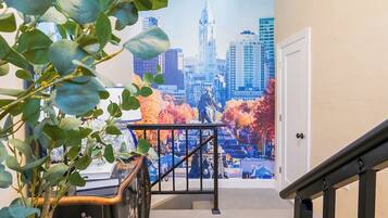 A staircase with a railing leading to a door, a wall with a cityscape mural, and a plant in the foreground.