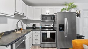 Una cocina moderna con gabinetes blancos, electrodomésticos de acero inoxidable, microondas, horno y refrigerador.