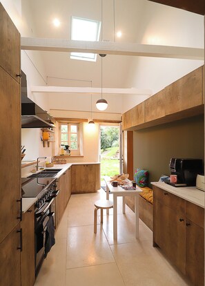 A modern kitchen with a central island, built-in oven, and a dining area with a table and chairs. - PENTY BRETON—Completely renovated / Sleeps 6–8, Finistère, Pointe du Raz, Cap Sizun (CLEDEN CAP SIZUN)