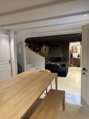 A modern interior with a wooden dining table, a sofa, and a staircase leading to a kitchen area.