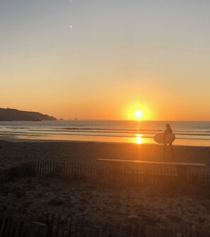 A beach scene with a person carrying a surfboard, waves, and a sunset.