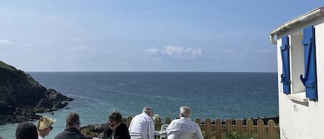 A coastal outdoor seating area with white plastic chairs and tables, overlooking the sea.