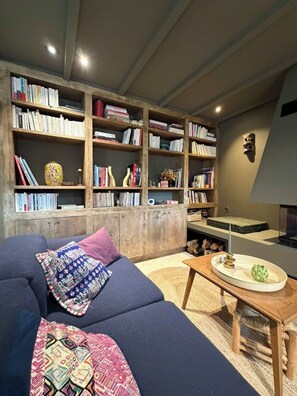 Una sala de estar acogedora con un sofá seccional, una estantería de madera llena de libros y una chimenea.