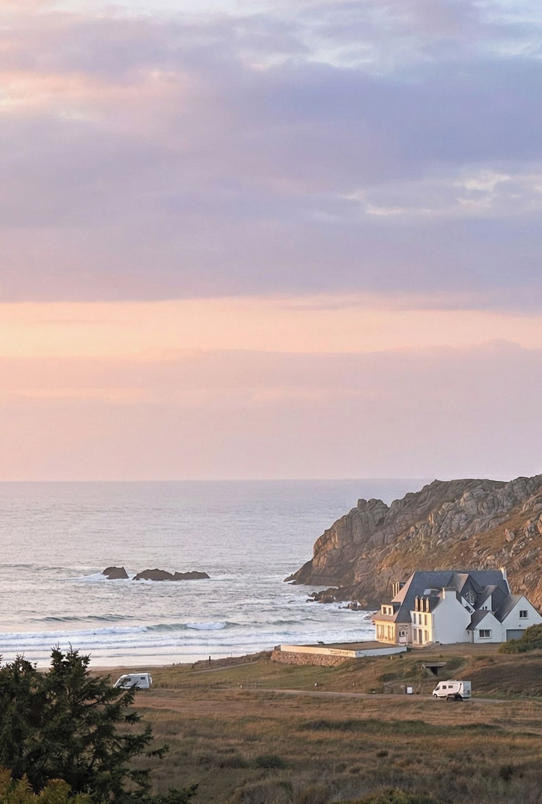 Une propriété située sur la côte, avec une maison près de la mer, un terrain rocheux et un ciel dégagé.