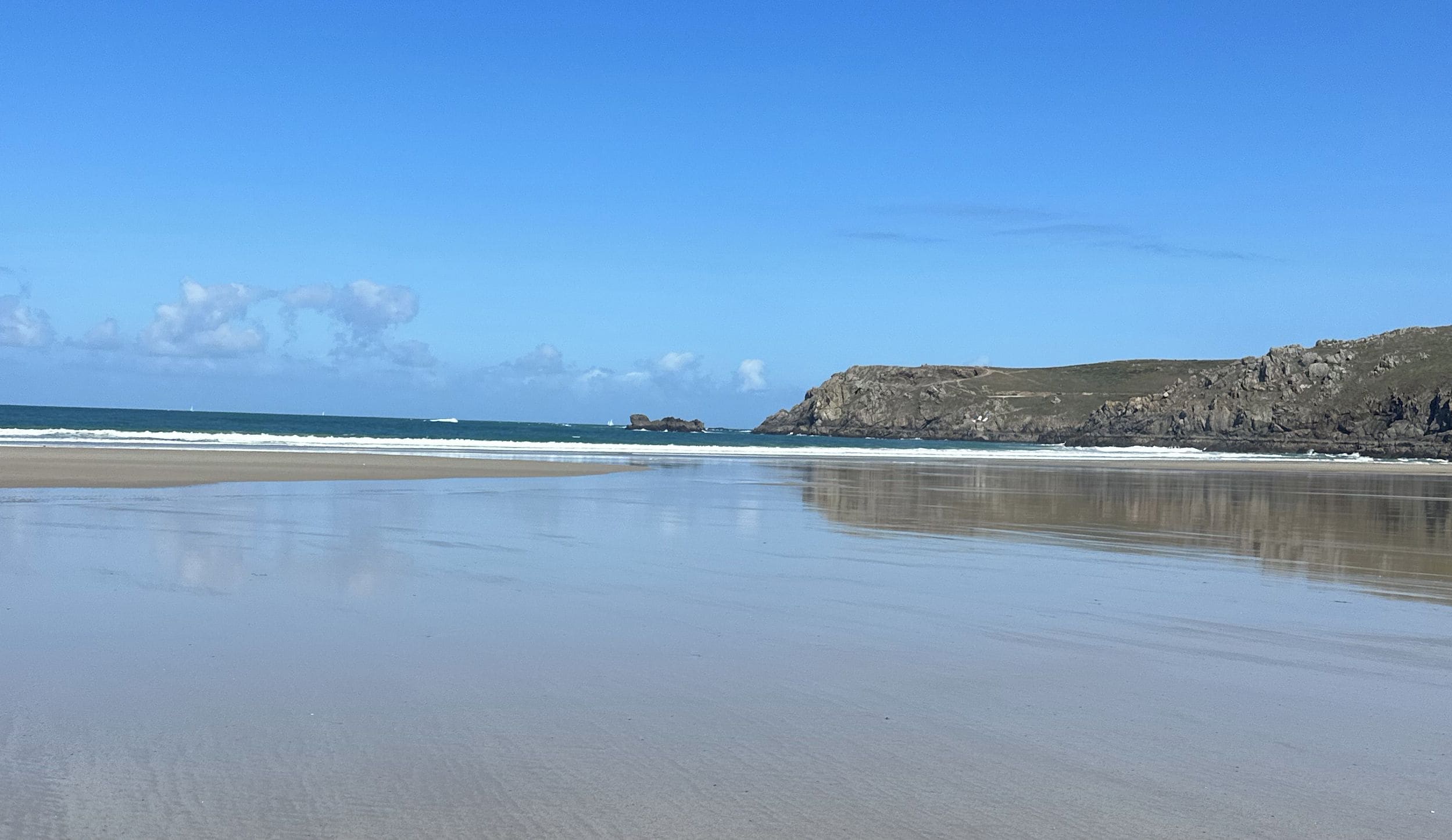 A beach with a rocky cliff and calm sea.