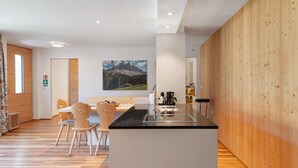 A modern kitchen with a wooden accent wall, a dining area with wooden chairs, and a painting of a mountain landscape. - Chalet 'Petrunderhof Sommertraum' with Mountain View, Shared Terrace and Wi-Fi (Villnöß)