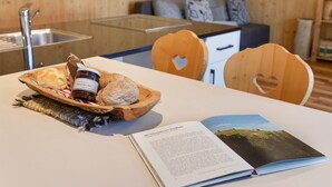 A wooden interior with a dining table, a book, and a wooden bowl with bread and jam. - Chalet 'Petrunderhof Sommertraum' with Mountain View, Shared Terrace and Wi-Fi (Villnöß)