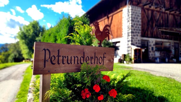 A wooden sign with 'Petrunderhof' written on it, surrounded by greenery and red flowers. - Chalet 'Petrunderhof Herbstparadies' with Mountain View, Shared Terrace and Wi-Fi (Villnöß)
