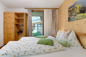 Un dormitorio con un armario de madera, una cama con ropa de cama floral, una almohada verde y un cuadro en la pared.