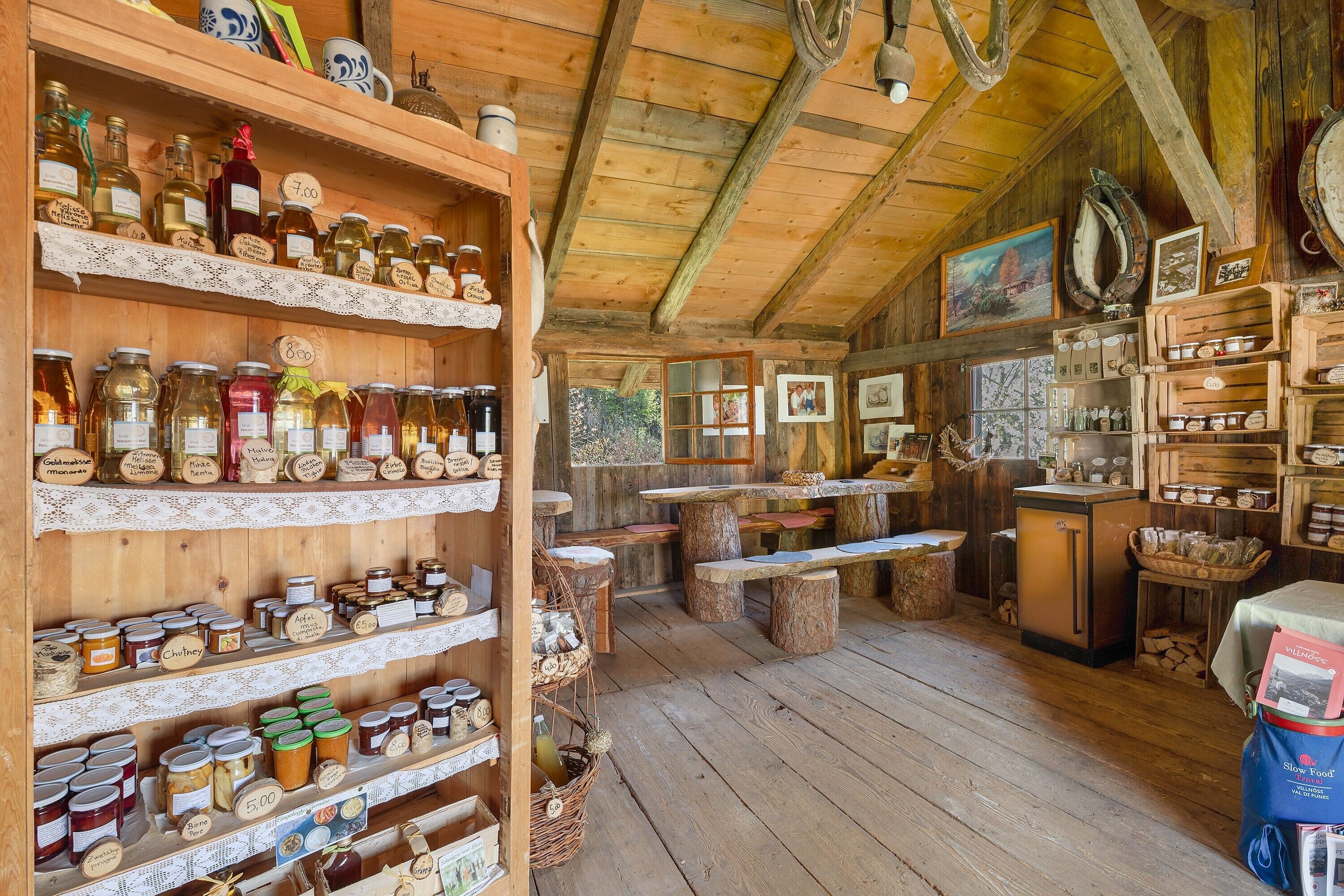 Un interno rustico con mensole di legno che espongono barattoli e bottiglie varie, un tavolo da pranzo in legno e un frigorifero.