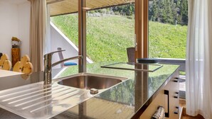 Een moderne keuken met een roestvrijstalen spoelbak, een houten aanrechtblad en grote ramen met uitzicht op een groene heuvel.