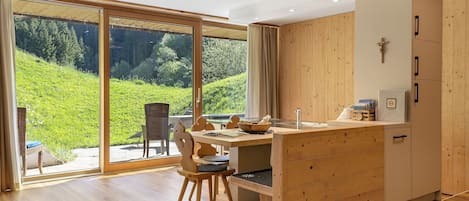 A modern kitchen with wooden cabinetry, a dining area with a table and chairs, and a large sliding glass door leading to a garden.