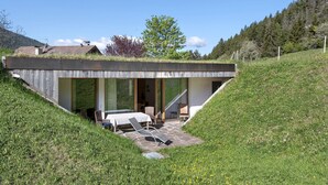 Een modern huis met een schuin dak, een terras met buitenmeubilair en uitzicht op het omliggende landschap.
