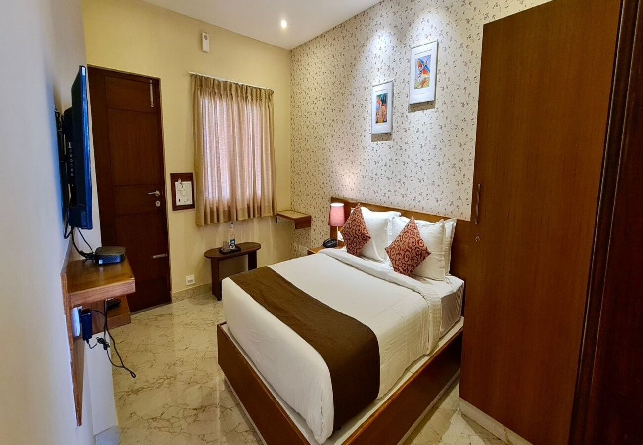 A hotel room with a bed, a TV, a bedside table, a lamp, a wardrobe, and a door.