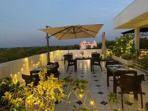 An outdoor dining area with tables and chairs, string lights, and a view of buildings in the background. - Villa Escape In (Vanur)