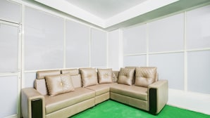 A beige sectional sofa with quilted pillows, a green carpet, and white walls with large windows. - Saver Single Karmanghat Midtown (Hyderabad)