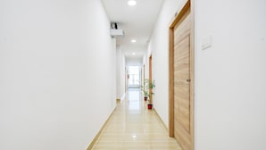A hallway with a wooden door, potted plants, and a ceiling-mounted air conditioning unit. - Saver Single Karmanghat Midtown (Hyderabad)