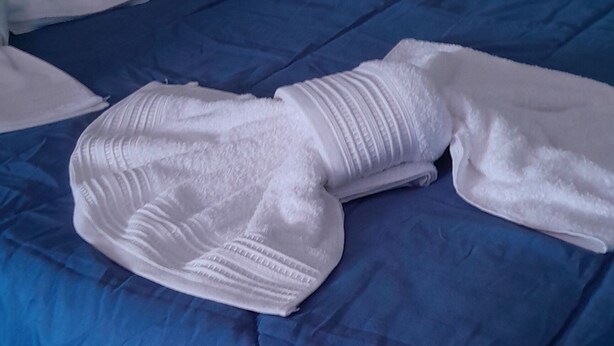 Una cama con una colcha azul y una toalla blanca doblada encima.