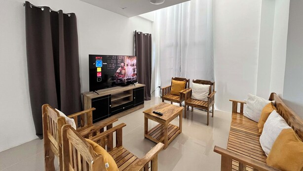 Un soggiorno moderno con TV a schermo piatto, mobili in legno e un'ampia finestra con tende.