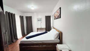 Una camera d'albergo con un letto in legno, un comodino con un asciugamano, un condizionatore d'aria a parete e un quadro.