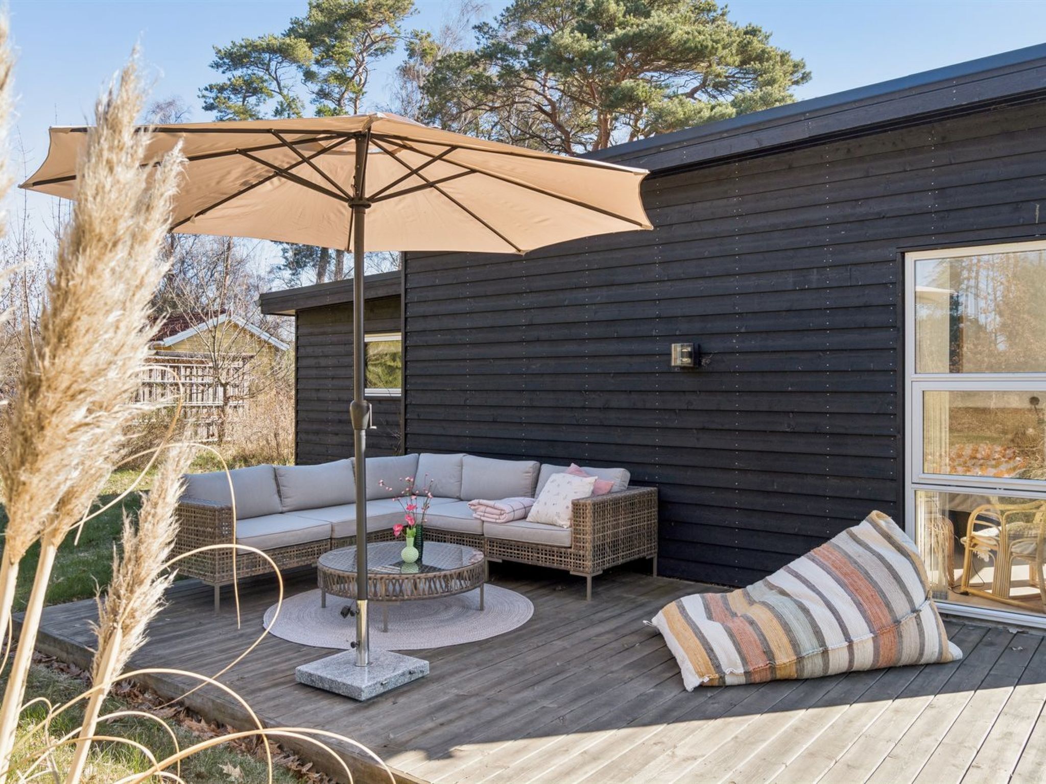 A modern outdoor seating area with a sofa, round table, and umbrella, surrounded by a wooden deck and a dark building facade.
