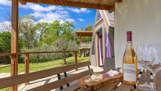 A wooden deck with a bench, a bottle of wine, and a glass on a table.