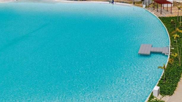 Una grande piscina a forma di curva con acqua cristallina, circondata da un percorso lastricato e qualche pianta.