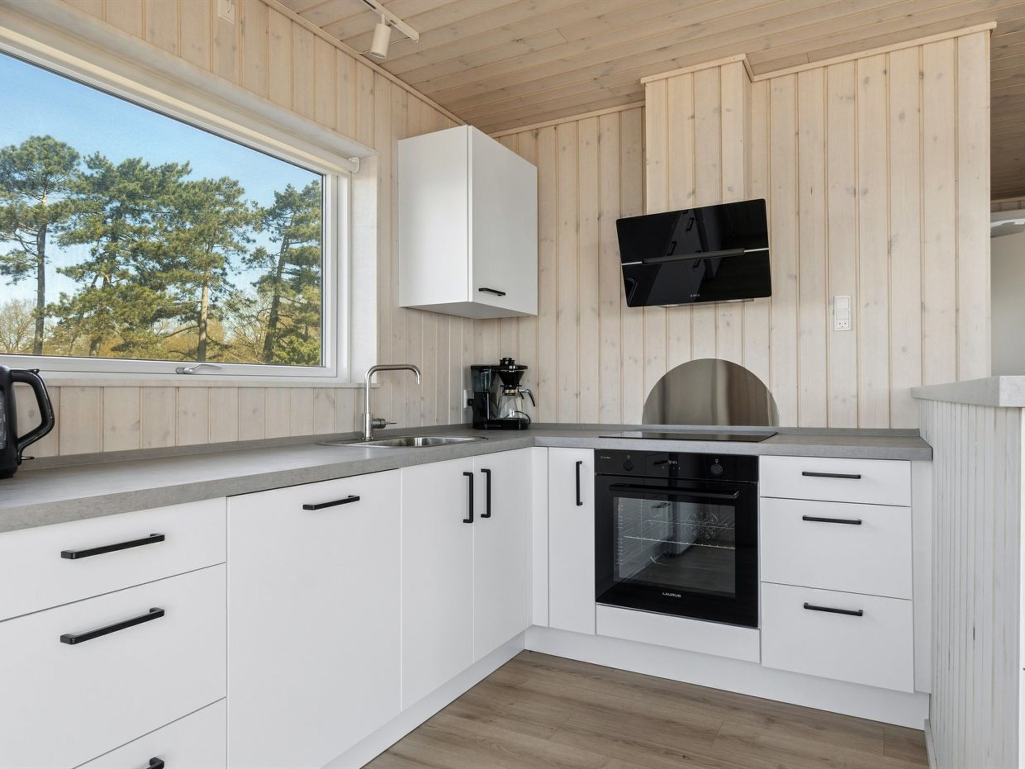 A modern kitchen with white cabinets, a built-in oven, a coffee maker, and a flat-screen TV mounted on the wall.