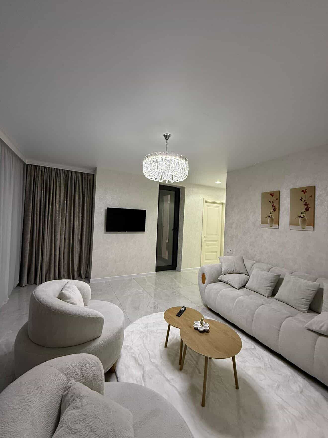 A modern living room with a chandelier, a sofa, a round coffee table, and a flat-screen TV.