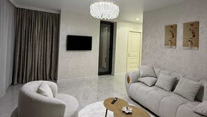 Uma sala de estar moderna com um candelabro, um sofá, uma mesa de centro redonda e uma televisão de tela plana.