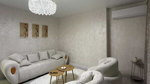Uma sala de estar moderna com sofá modular, pufes redondos, mesa de centro de madeira e um lustre.