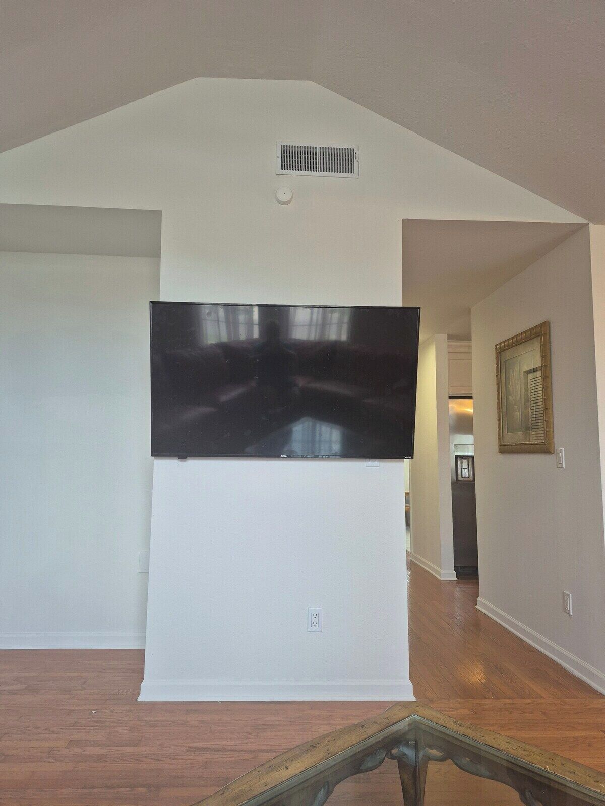 A living room with a flat-screen TV mounted on the wall, hardwood flooring, and a staircase leading to another level.