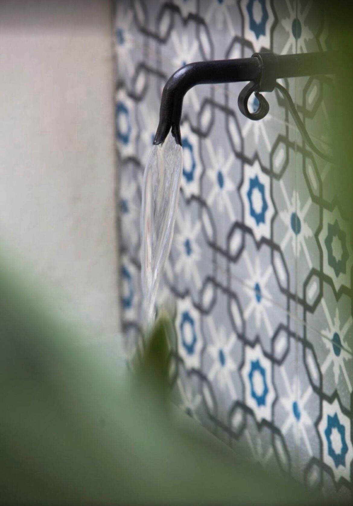 Un grifo con agua corriendo, una pared con diseño y un objeto verde parcialmente visible.