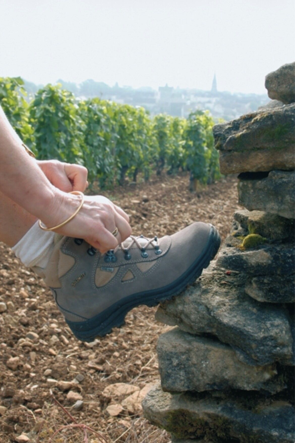 A hand holding a hiking boot over a stack of rocks.