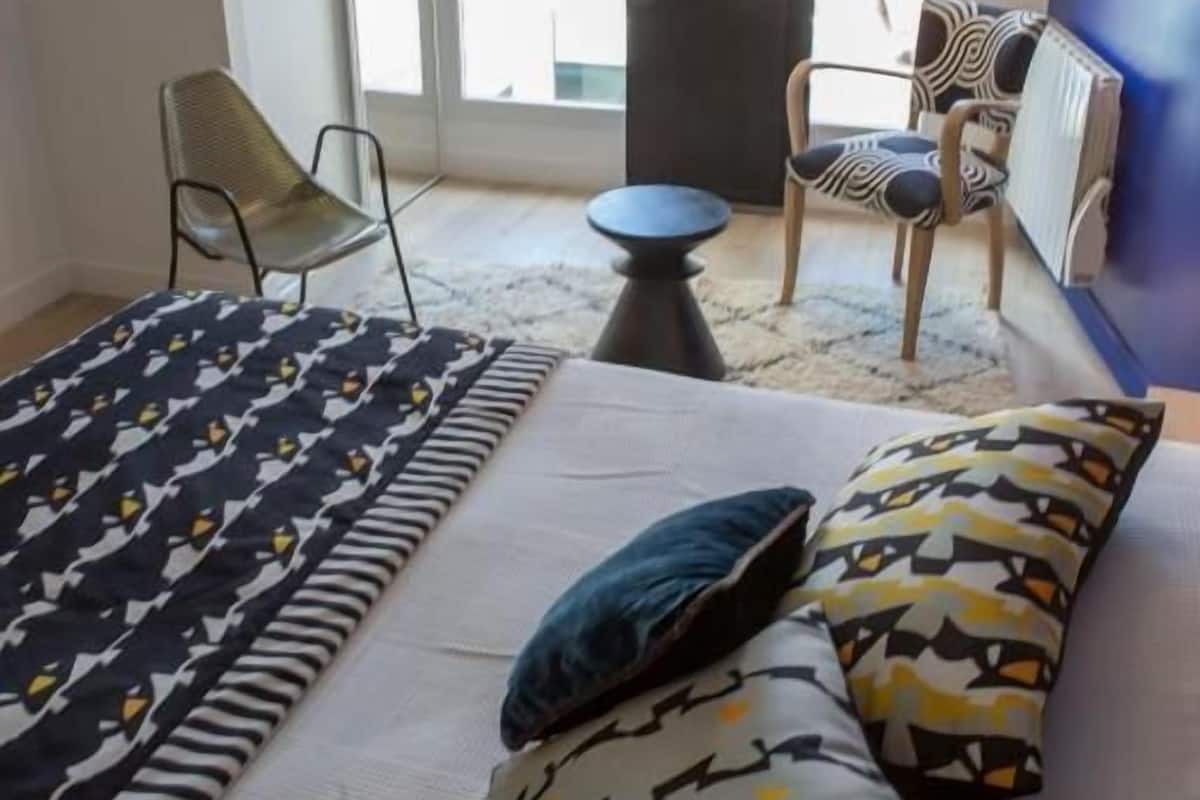 Una camera d'albergo con un letto, due sedie, un tavolino e vista attraverso una porta vetrata.