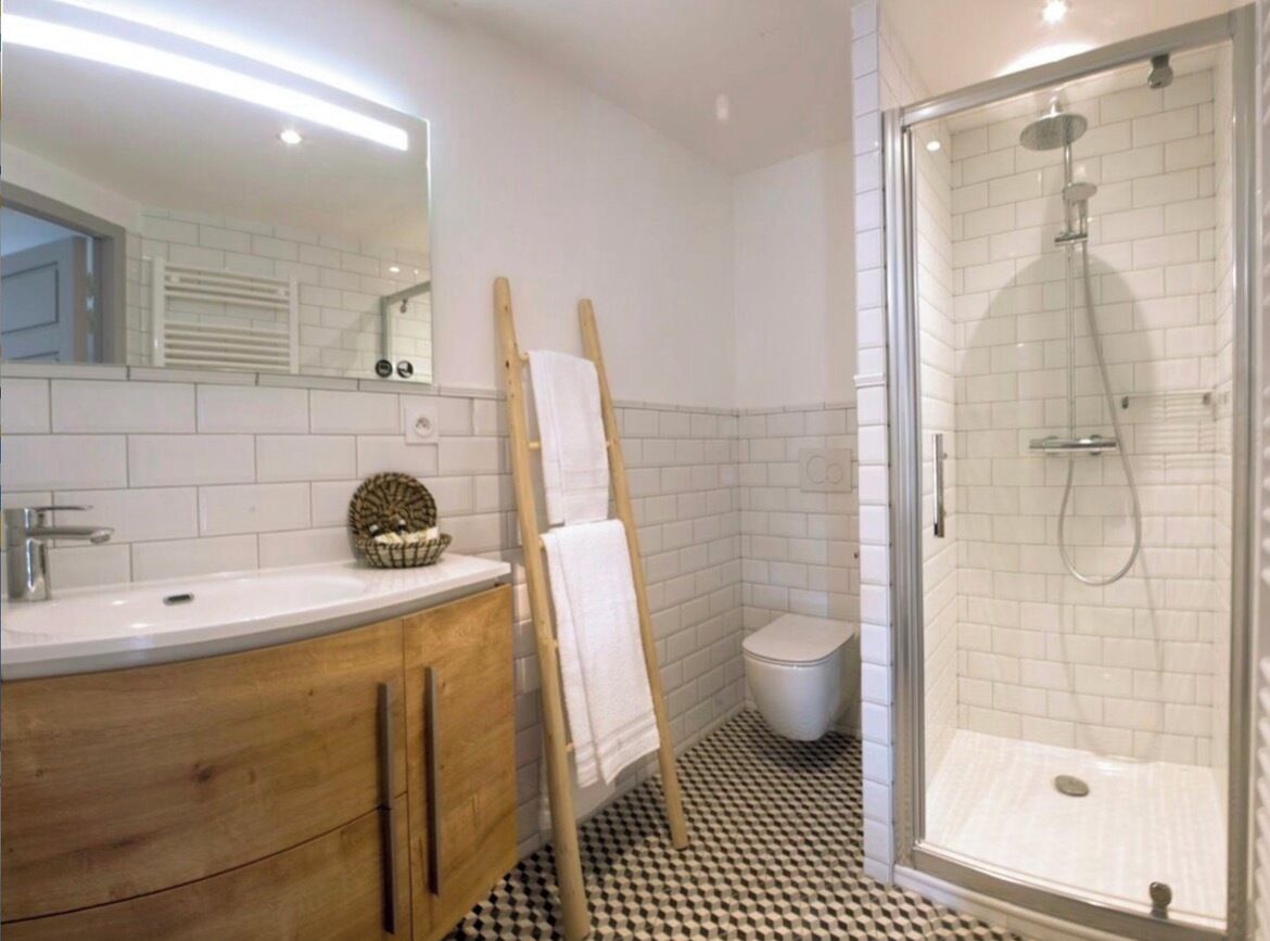 A bathroom with a white sink, wooden vanity, a towel rack, a toilet, and a glass-enclosed shower.