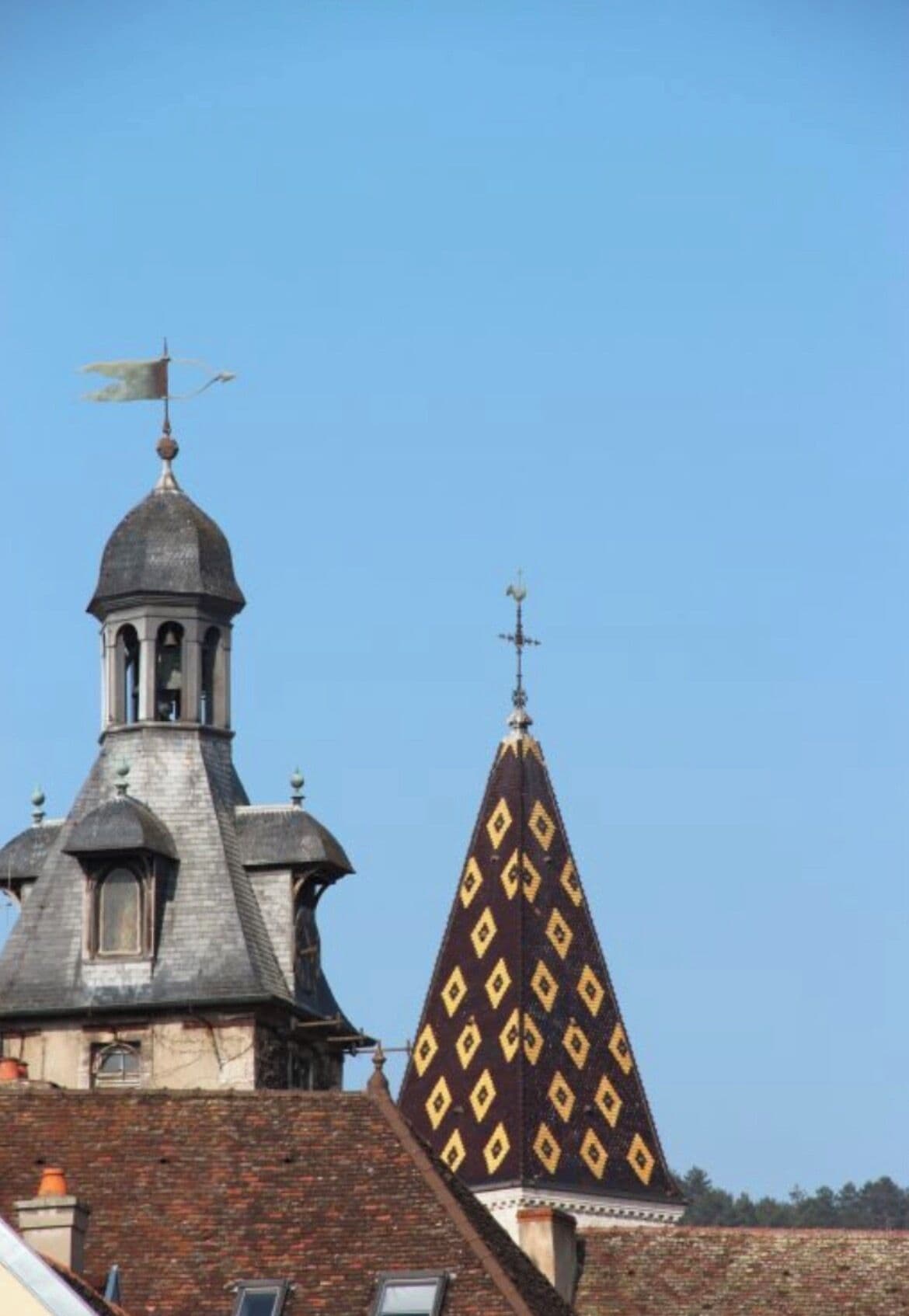 Een gebouw met een opvallende toren, voorzien van een windvaan en een puntig dak met ruitmotieven.